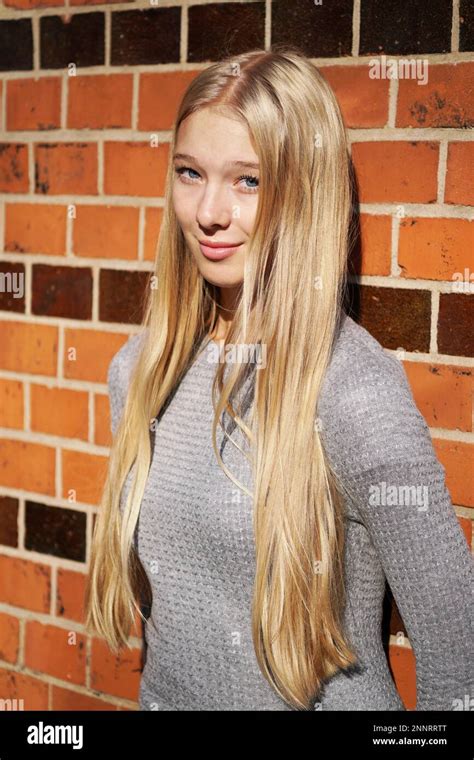 Teenage Girl With Long Blond Hair Leaning Against Brick Wall Stock