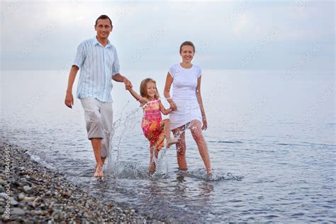 Happy family with little girl splashes feet water on beach Stock Photo ...