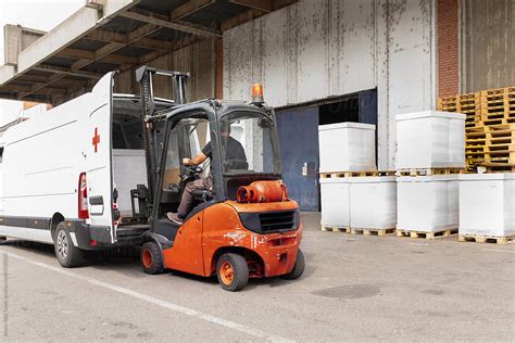 The Worker Transports Freight Into A Van Using A Forklift By Stocksy