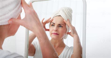 Forty years old woman looking at wrinkles in mirror. Plastic surgery