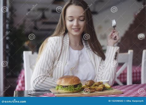 Brunette Girl With Long Hair In A Restaurant Appetizing Eating Burger And Fried Potatoes In The