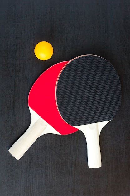 Duas raquetes de tênis de mesa ou ping pong e bola em um fundo preto