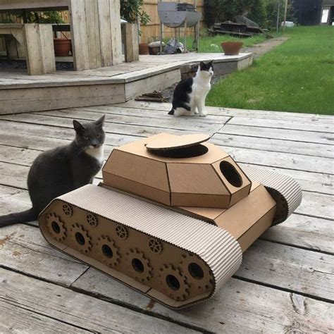 A Cat Sitting On A Deck Next To A Cardboard Tank And Another Cat