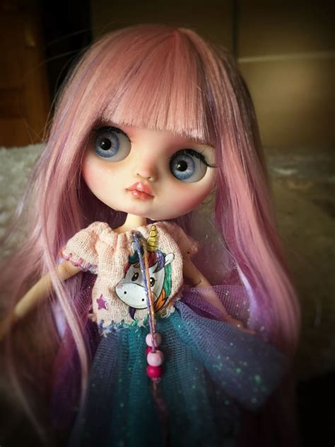 A Close Up Of A Doll With Pink Hair And Blue Eyes Wearing A Dress