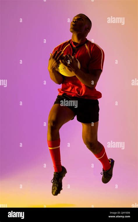 African American Male Rugby Player With Rugby Ball Over Pink Lighting