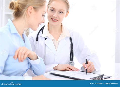 Blonde Female Doctor And Patient Talking In Hospital Office Health Care And Client Service In