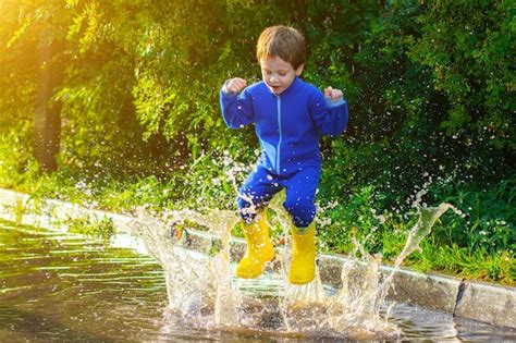 Premium Photo A Happy Boy In Rubber Boots Jumps In Puddles The Boy