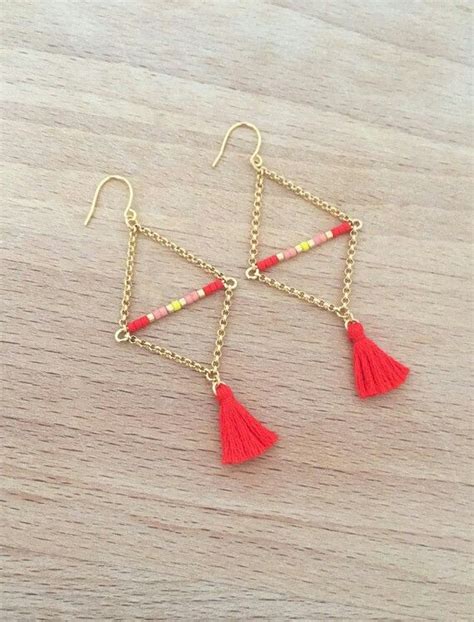 Red Tasseled Earrings With Gold Chains And Beads On A Wooden Surface