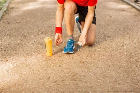 Handsome Young Runner Tying Shoelaces On The Track In The Spring Park