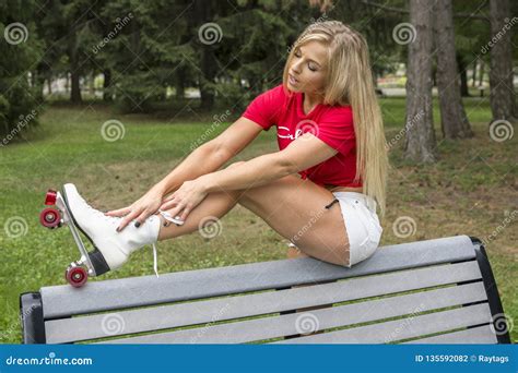 Mooie Jonge Vrouwenzitting Op Een Parkbank Met Rollerskates Stock Foto