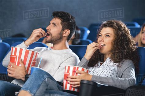 Couple Eating Popcorn While Watching Film Together In Cinema Stock