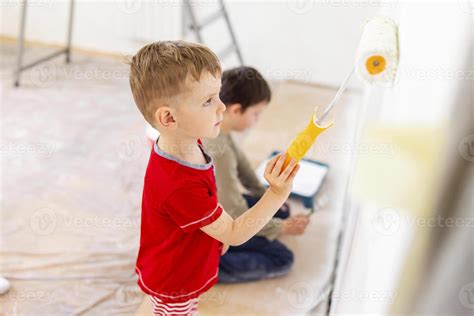 Children paint a wall with brush and roller in white color. Children ...