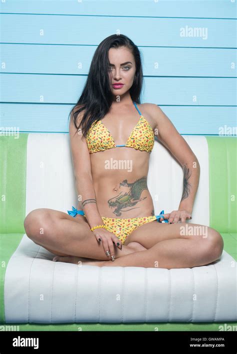 Beautiful Brunette Woman Wearing Yellow Bikini Looking Into The Camera While Sitting On The