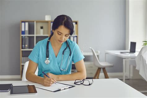 Médico Joven Serio Sentado En El Escritorio Y Completando La