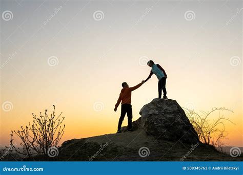 Man And Woman Hikers Helping Each Other To Climb A Big Stone At Sunset