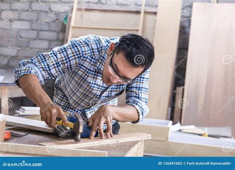 Worker At Carpenter Workspace Installing Nail Using Hammer Stock Photo