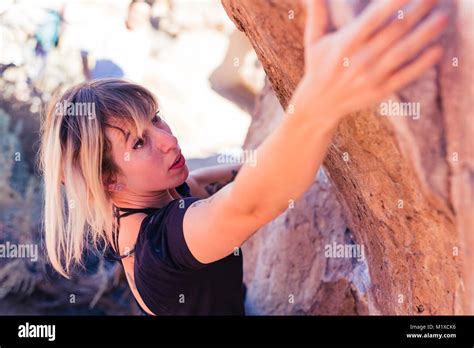 Dünne blonde kaukasische Frau mit Arm tattoos Rock klettert auf Felsbrocken in der Wüste von