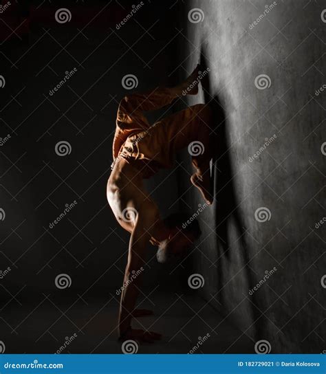 Aged Male With Naked Torso In Brown Pants Is Practicing Yoga Standing On Hands Leaning