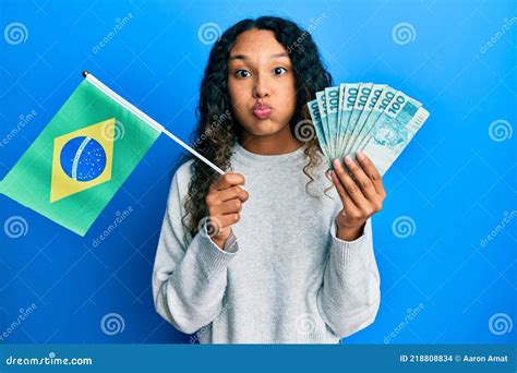 Joven Latina Con Bandera De Brasil Y Billetes Reales Hinchando Mejillas Con Cara Divertida Foto