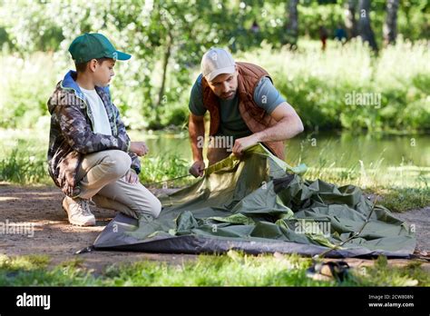 Full Length Portrait Of Father And Son Setting Up Tent Together While