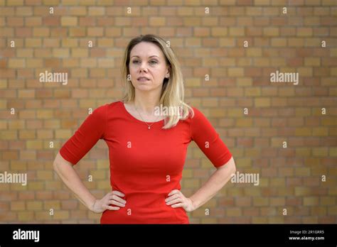 Pensive Attractive Middle Aged Blonde Woman In Front Of A Wall Wearing A Red Top Has Her Hands