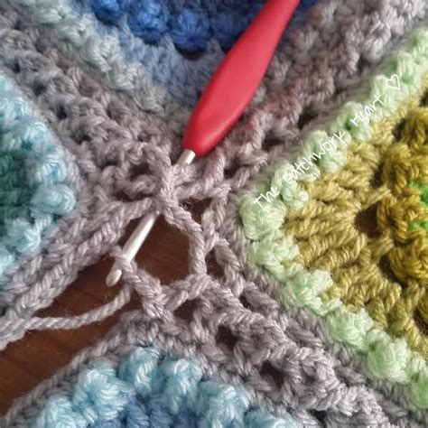 A Crocheted Granny Blanket With A Red Handled Knitting Needle On Top Of It