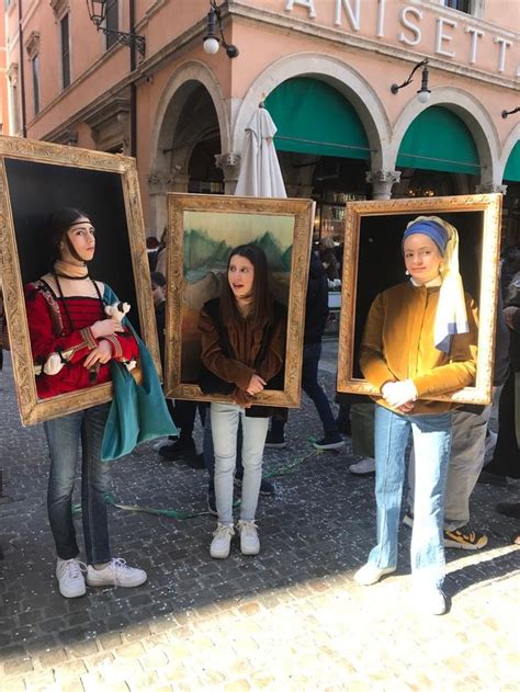 Three Women Holding Paintings In Front Of A Building With People