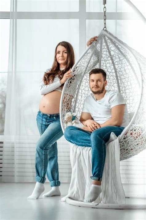 A Pregnant Girl With Her Husband Are Standing In A Bright Bedroom