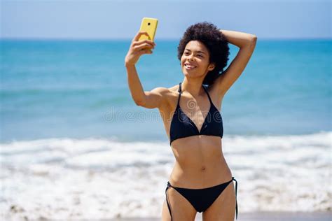 Content Black Woman In Bikini Taking Selfie On Beach Stock Image