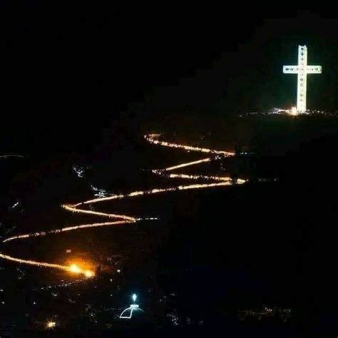 A Large White Cross On Top Of A Hill At Night With Lights All Around It