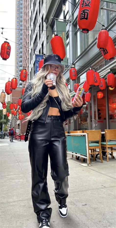 a woman in leather pants and a hat holding a cell phone