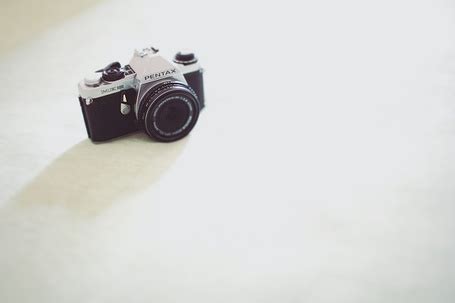 Фото Фотоаппарат PENTAX, лежащий на бревнах