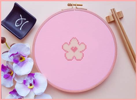 A Pink Cross Stitch Pattern With Flowers And Chopsticks Next To It