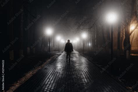 Sad man alone walking along the alley in night foggy park. Back view Stock Photo | Adobe Stock