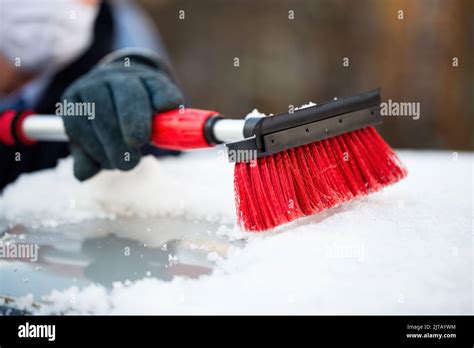 Man In Gloves Removing Snow From A Roof Of A Car With Red Brush Stock