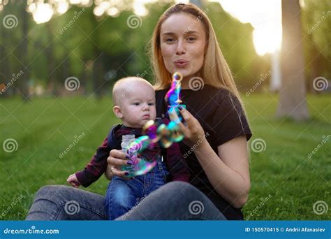 Young Caucasian Mother Inflates Soap Bubbles With Her Little Son In A