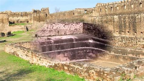 an old stone bathtub in the middle of a grassy area next to brick walls