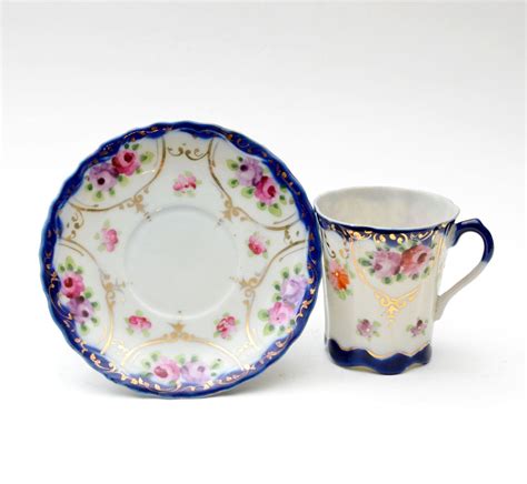 Two China Cups And Saucers One With Flowers On The Rim Is Sitting Next