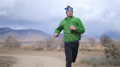 A Handsome Gay Man Is Jogging Along A Dirt Road In A Green Jacket And With A Blue Bandana On His