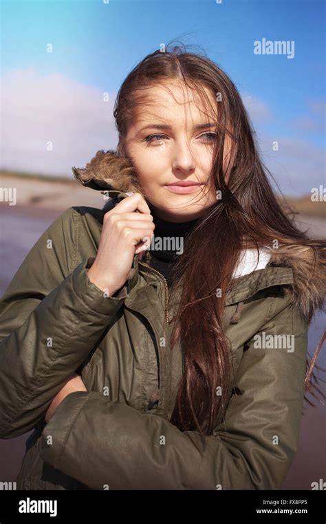 Beautiful Young Woman Huddling In Her Coat On A Windy Day At The Beach