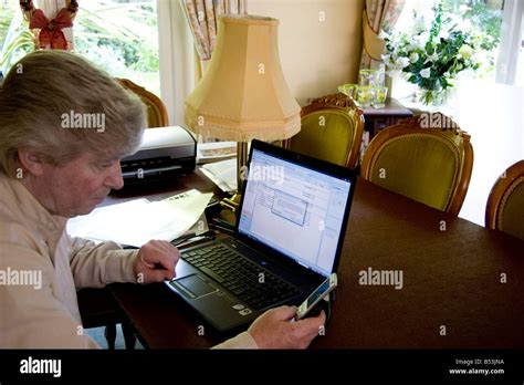 Mature Caucasian Man Sitting In Front Of His Laptop Using His Mobile Phone Stock Photo Alamy