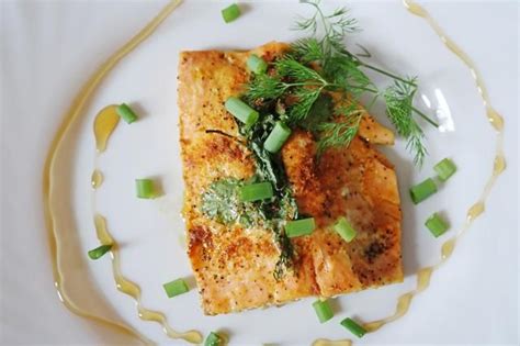 A White Plate Topped With Fish Covered In Green Vegetables