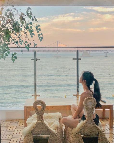 A Woman Sitting On Top Of Two Wicker Chairs Next To The Ocean With A