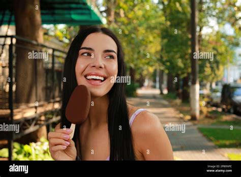 Beautiful Young Woman Eating Ice Cream Glazed In Chocolate On City