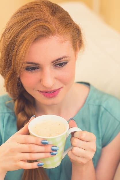 Pelirroja sonriente sentada en el sofá tomando café Foto Premium