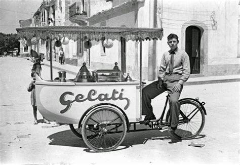 An Old Photo Of A Man On A Bike With A Cart In The Back That Is Selling