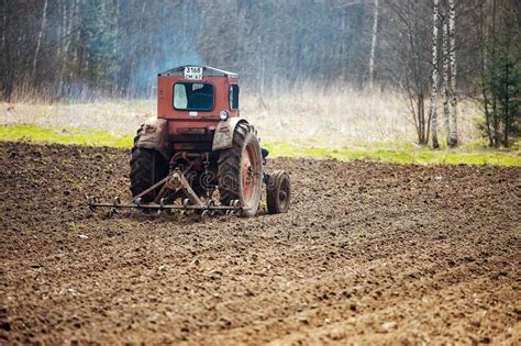 An Agricultural Tractor Plows The Land In A Field In The Spring Stock