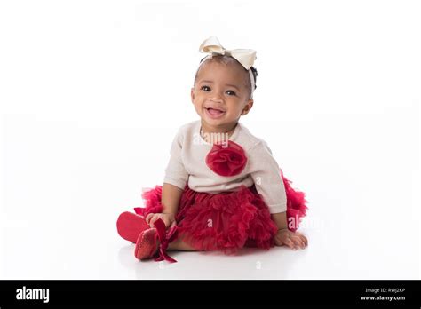 A smiling six month old baby girl wearing a red tutu. She is sitting on ...