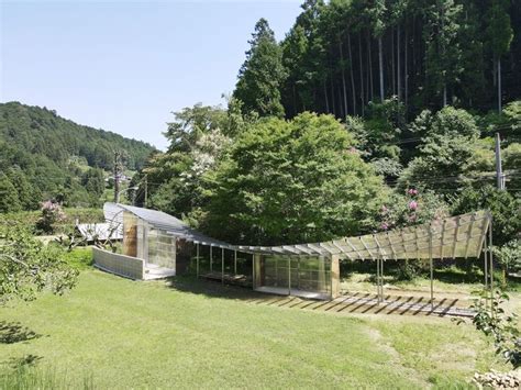 A Glass House In The Middle Of A Lush Green Field With Lots Of Trees