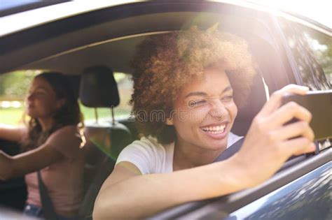 Two Female Friends Or Same Sex Couple In Car On Road Trip Vacation Taking Picture On Mobile
